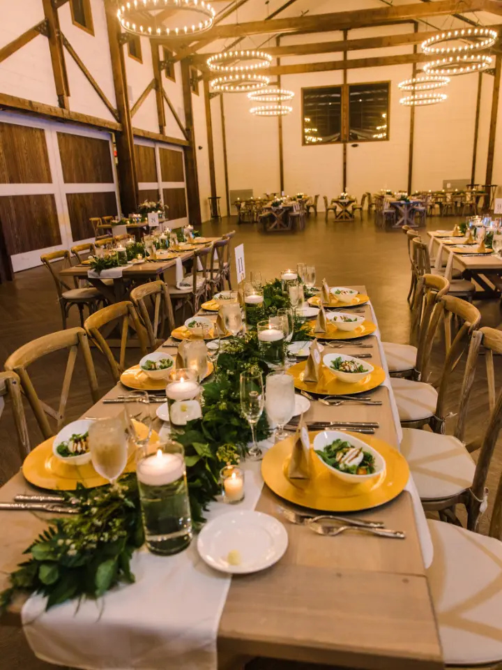 Table setting with a row of greenery down the middle with bright gold chargers and candles