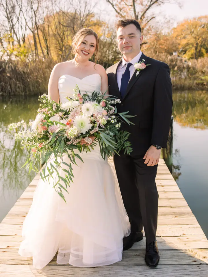 Bride and Groom standing on a dock at Kent Island resort, bride holding a large than life pastel bouquet with lots of greenery by Wildly Native Flower Farm
