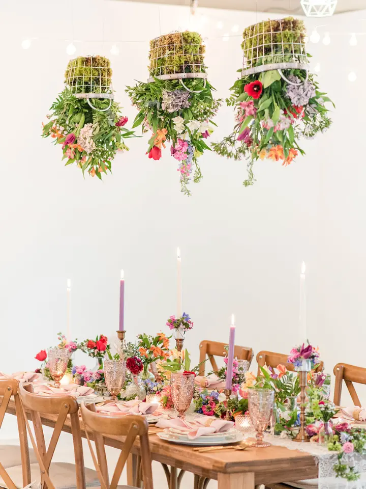 hanging floral basket installation over a honey oak farmhouse table with candles and brightly colored flowers