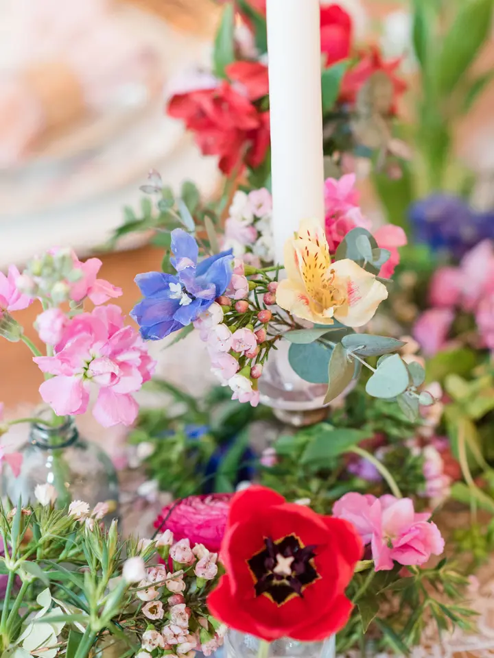 Up close of a candle surrounded by brightly colored small flowers 
