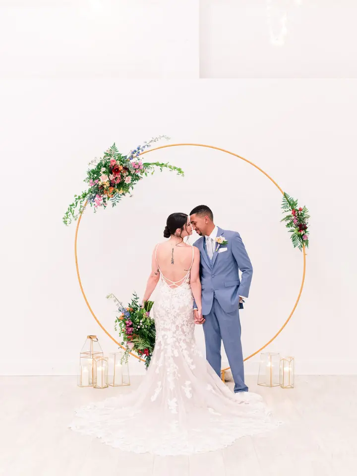Bride and Groom looking at each other within a gold circle arch with a greenery piece attached
