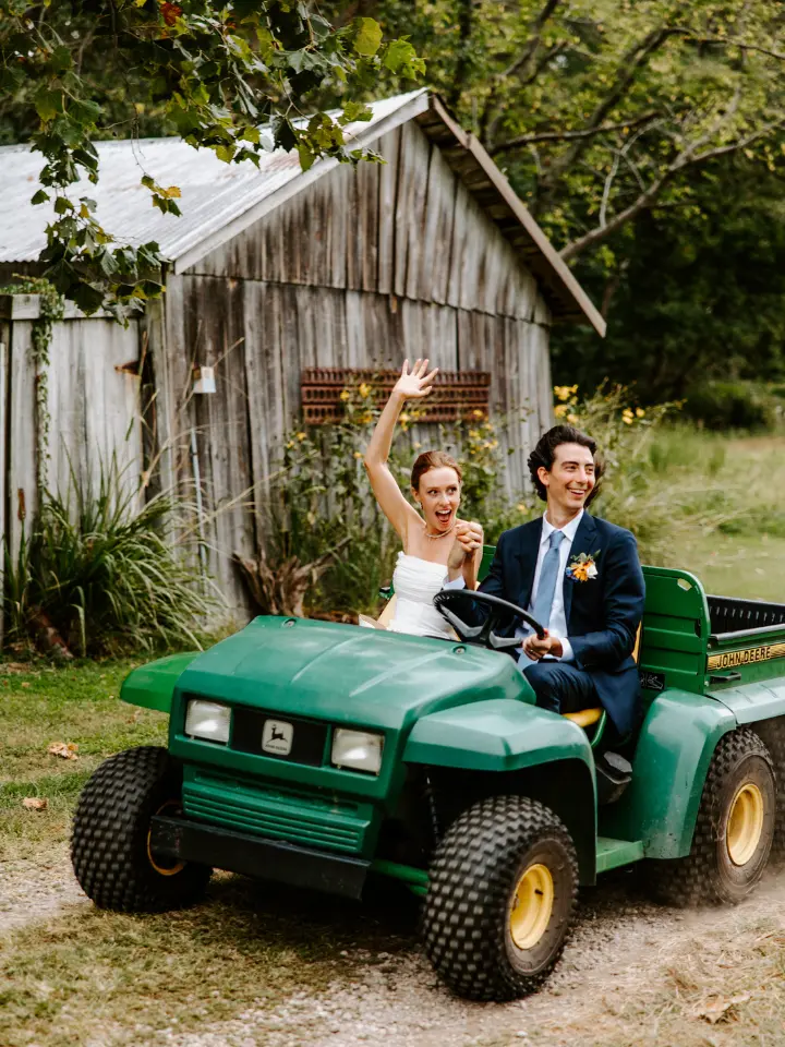 Bride and Groom waving and looking away from the camera while riding a Gator (golf cart)