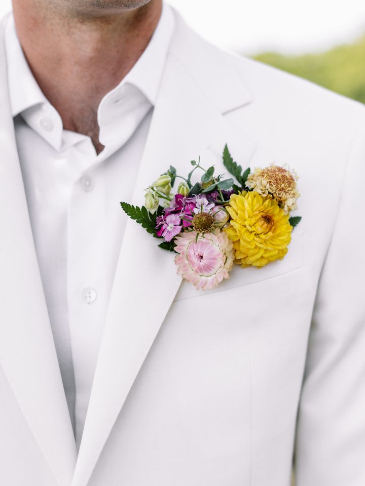 Cloesup of summery bright flowers in a pocket square on a white suit.