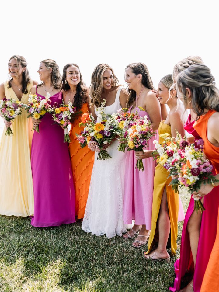 Bride and bridesmaids pose in a line outside on the grass.