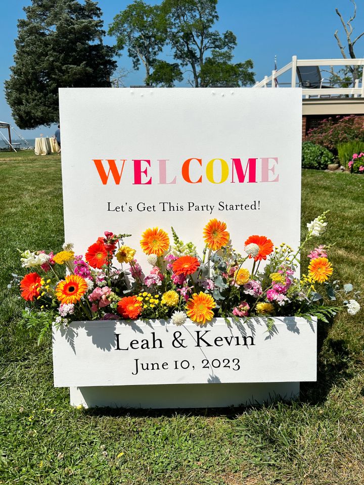 Bright white welcome sign with citrus colors lettering and flowers for a summer wedding.