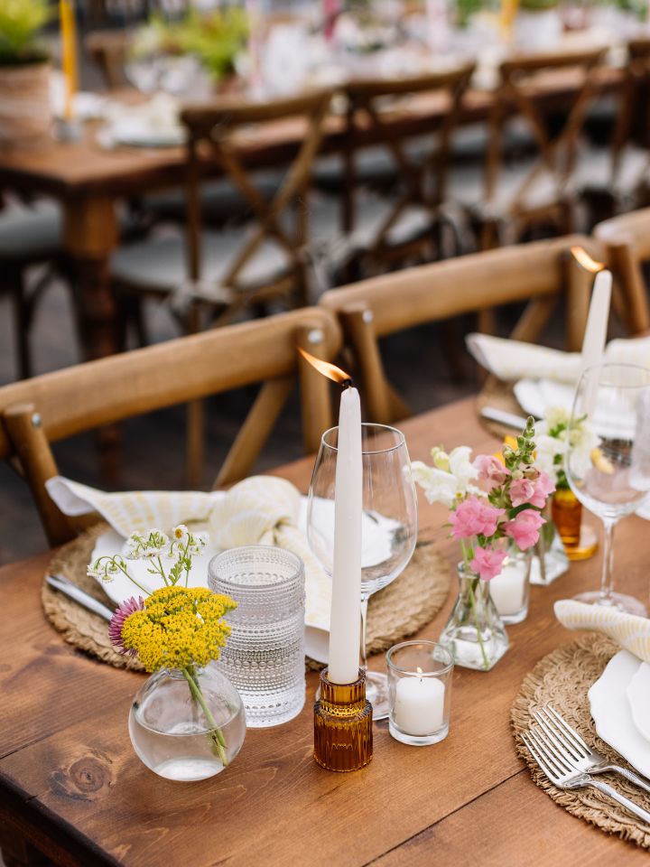 Taper candles and bud vases on a wooden reception table.