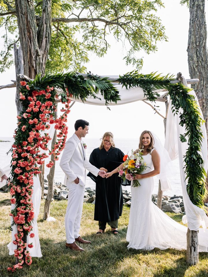 Bride and groom stand under a floral chuppah.