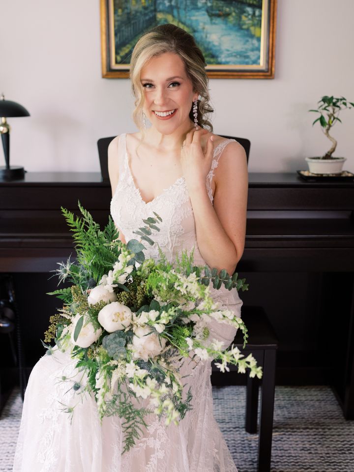 Brides sits and holds her bouquet of white flowers, smiling.