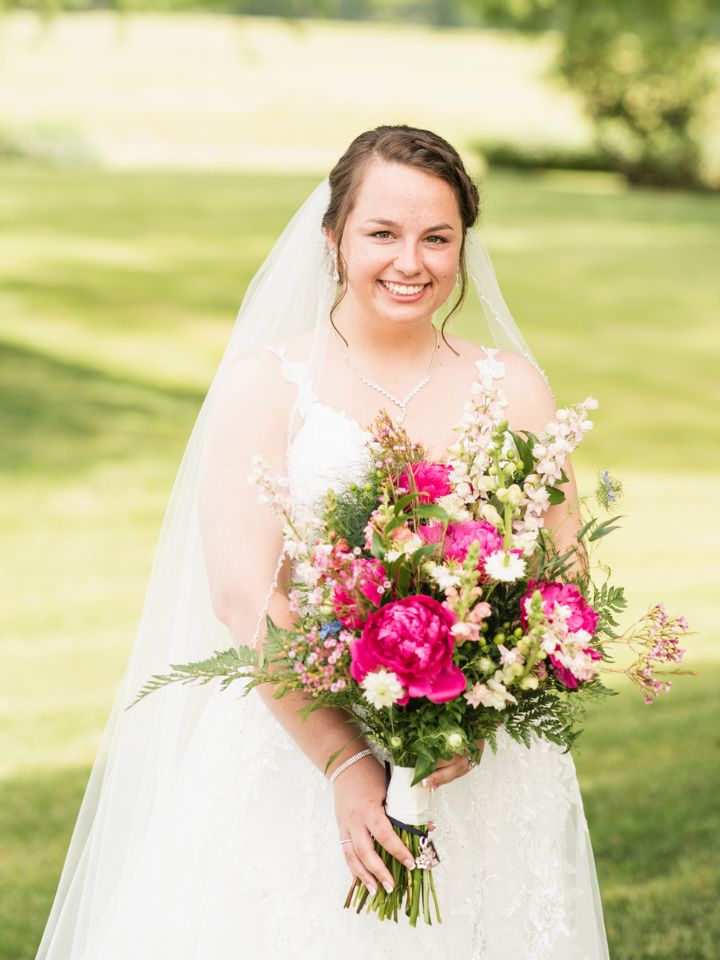 Bride holds her pink floral bouquet and smiles.