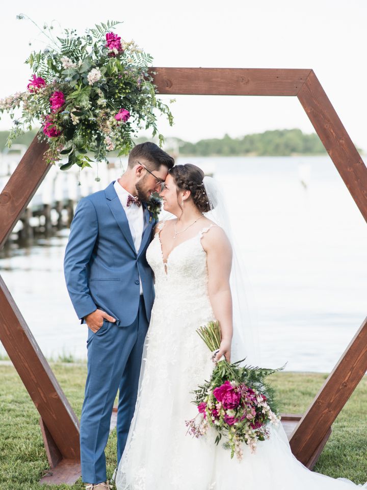 Bride and Groom stand under a wooden hexagon arch holding spring wedding flowers.