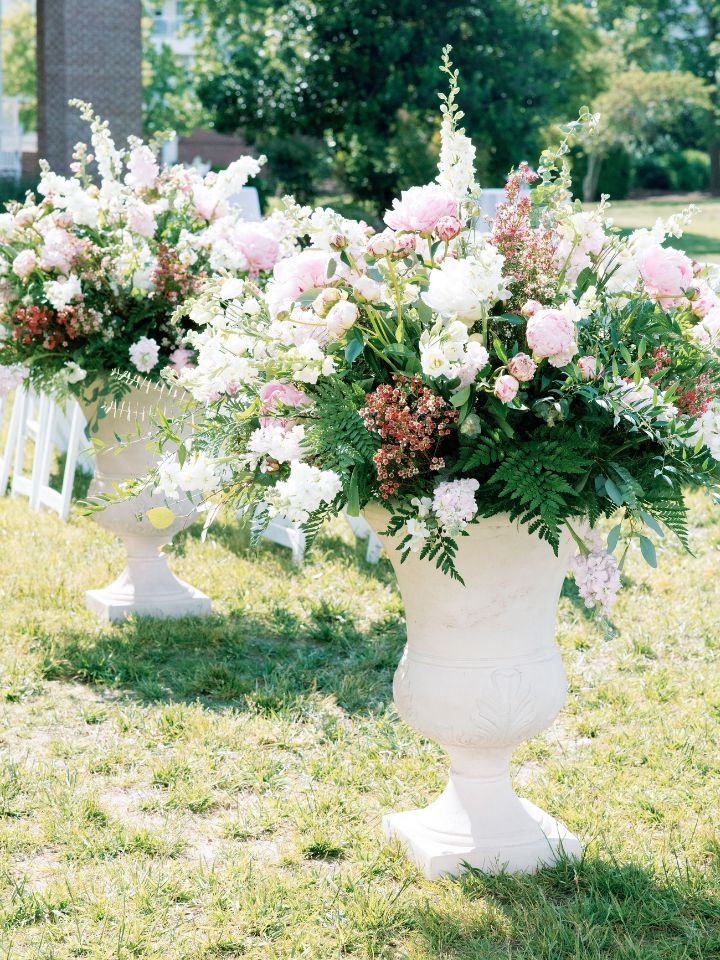 Large cement urns hold overflowing floral arrangements in pink and white