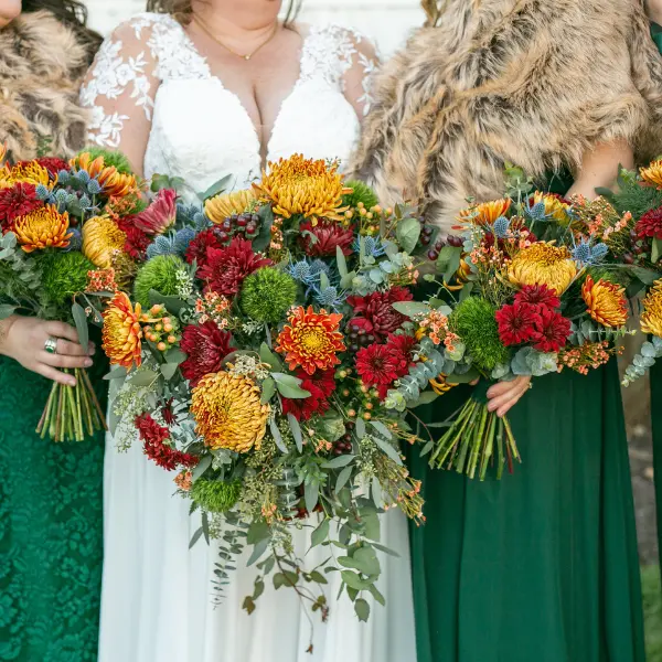 Up close view of a bride and her bridesmaids in green with orange, yellow, and red bouquets for a fall wedding