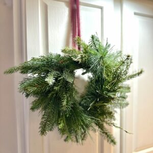 Mini greens wreath hangs from a burgundy ribbon on a white kitchen cabinet.