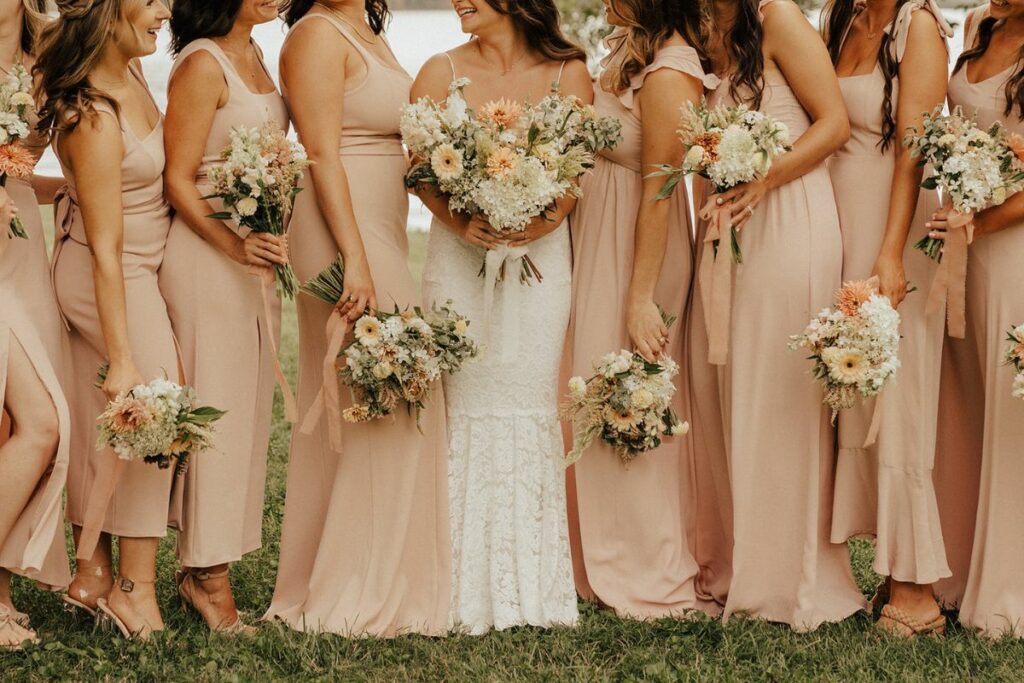 Bridesmaids in pastel dresses and holding bouquets of peach and white flowers