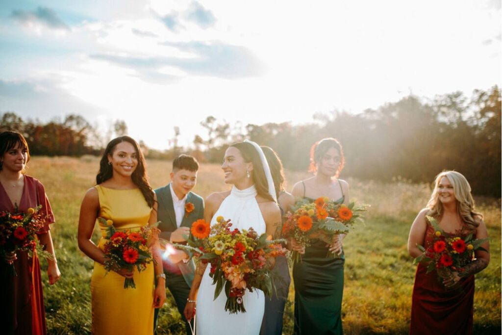 Bride and bridal party in a field at Hazelwood Weddings holding orange flower autumn bouquets