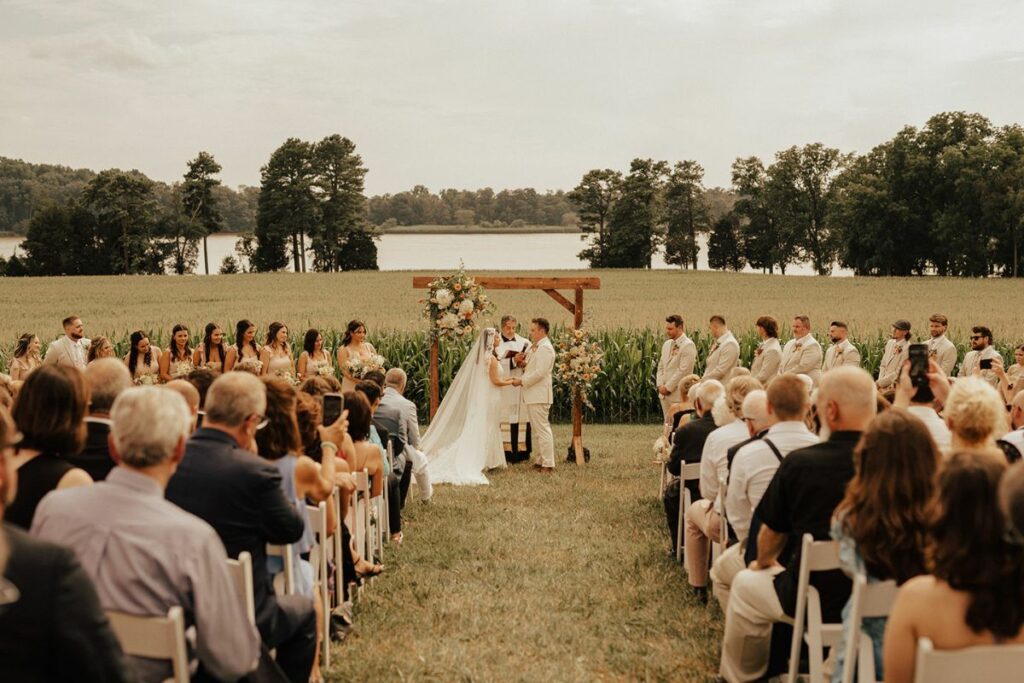 Bride and groom stand at end of aisle under wooden arch from Wildly Native during wedding ceremony at Brittland Manor