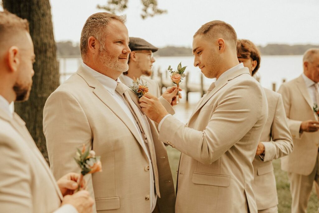 Groomsmen pin on pastel flower boutonnieres on neutral tan suits