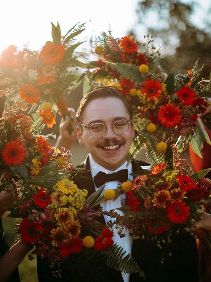 Groom smiles surrounded by bridesmaids' bouquets