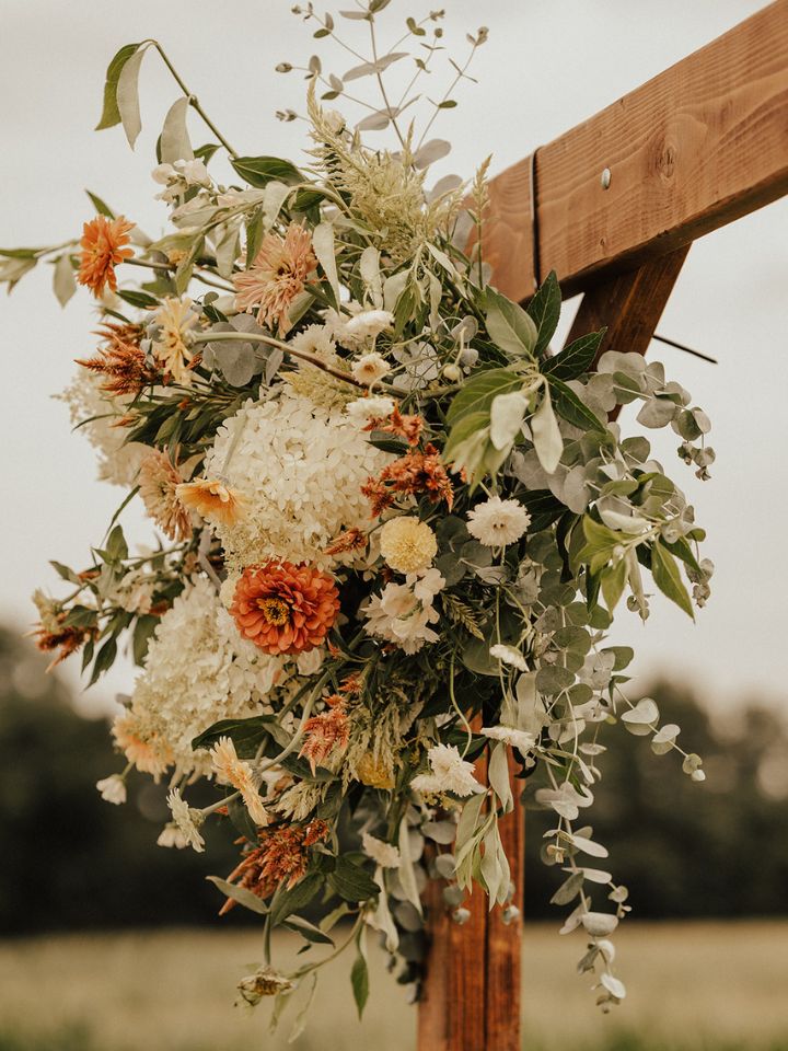 Close up of pastel peach and white flowers decorating the corner of a wooden wedding arch