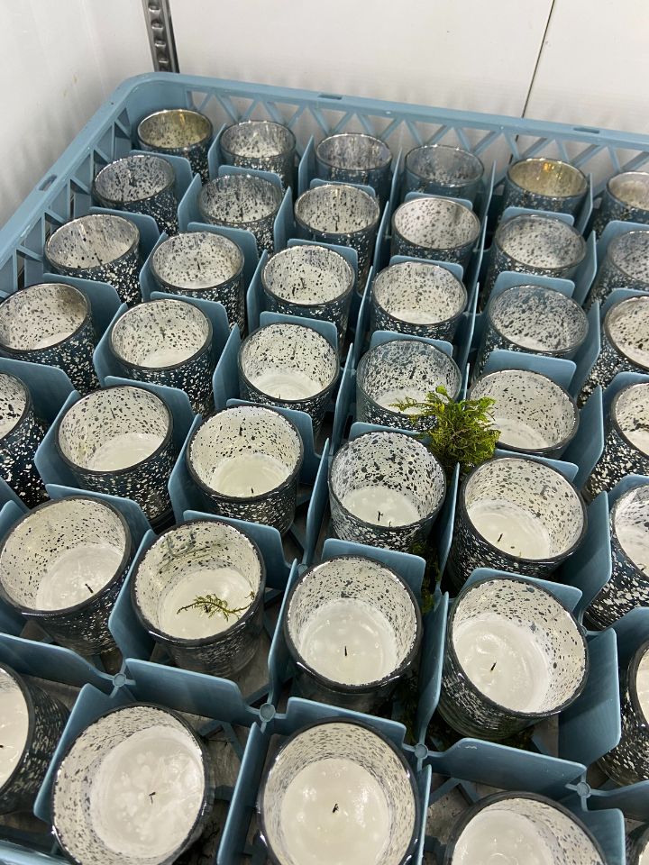 A rack of used votice votive candles sits in a floral cooler.