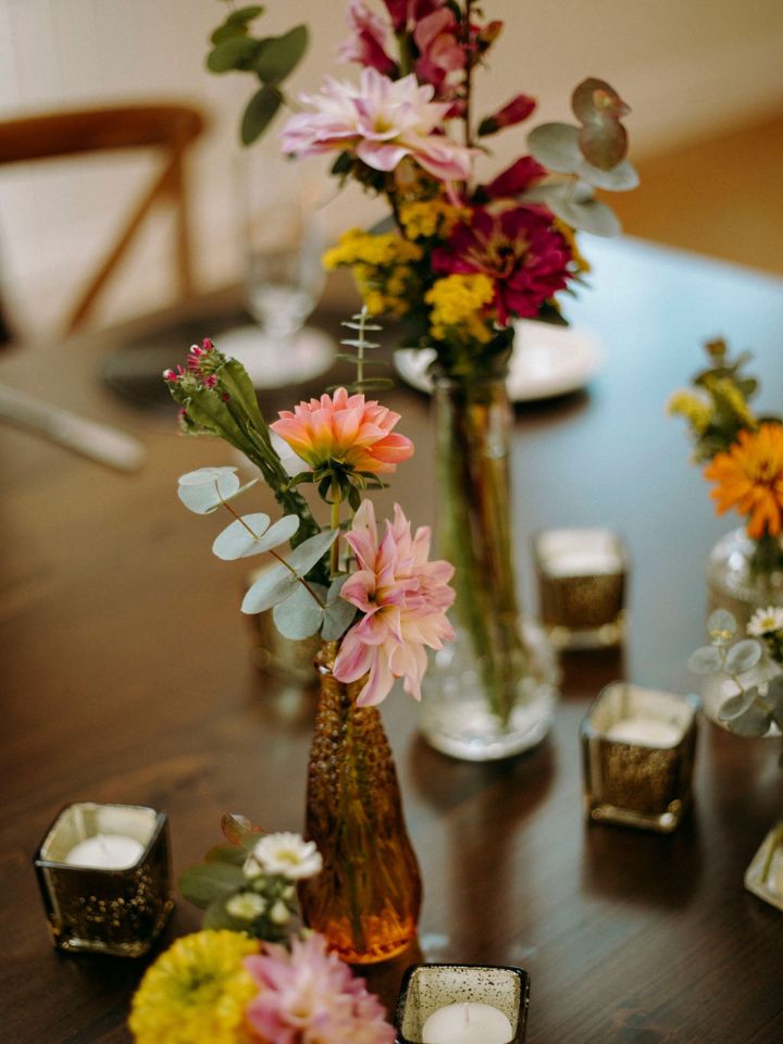 Bud vases with orange, peach, and red flowers on a table with retro vibes square votive candles