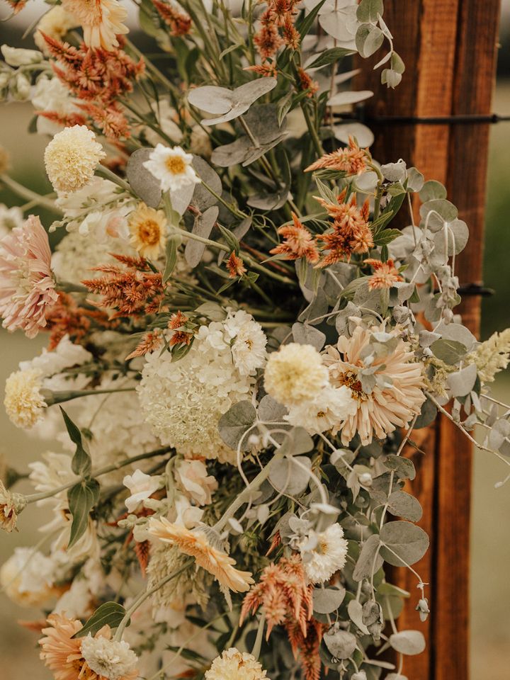 Pastel white, yellow, and peach flowers and eucalyptus on wood wedding arch