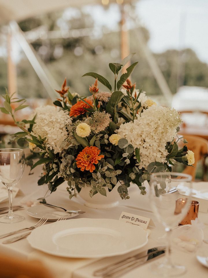 White compote filled with orange flowers and white hydrangeas on guest tables