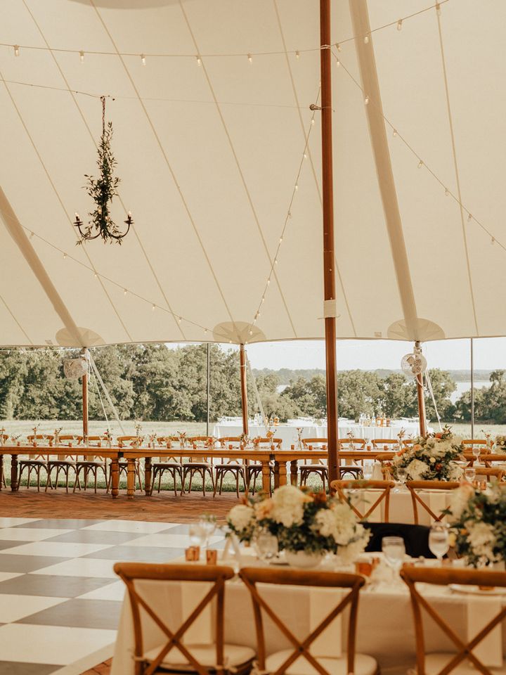 White sailcloth tent for tented wedding reception at Brittland Manor. Long rectangle tables for guest seating with big flower arrangements. Chandeliers in tent decorated with greenery