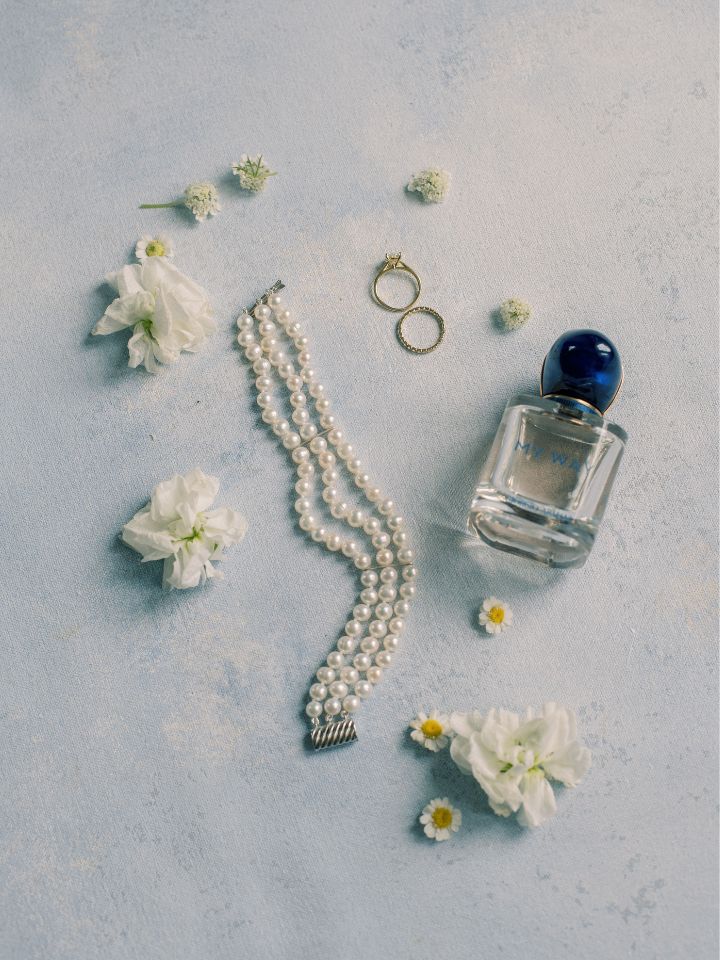 White flowers, white pearl choker, wedding rings, and blue perfume