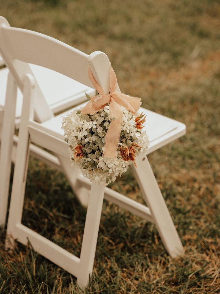 White folding chair with pastel peach ribbon & a ball of flowers decorating it