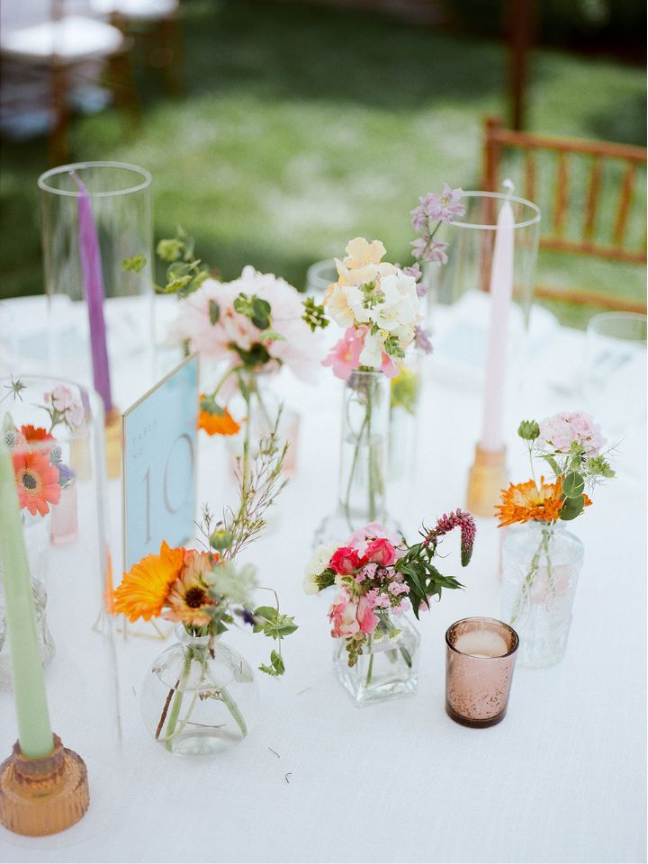 A table set with white tablecloth, flower vases, taper candles, and votive candles.