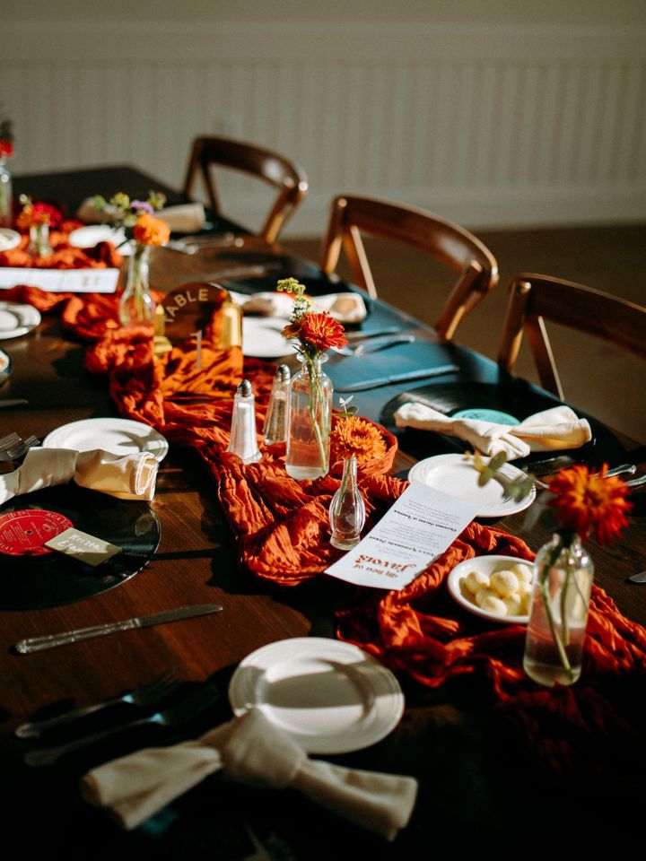 Long table for wedding guests decorated with orange chiffon and bud vases with orange flowers