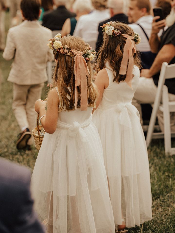 Two flower girls wear white dresses and pastel colored flower crowns