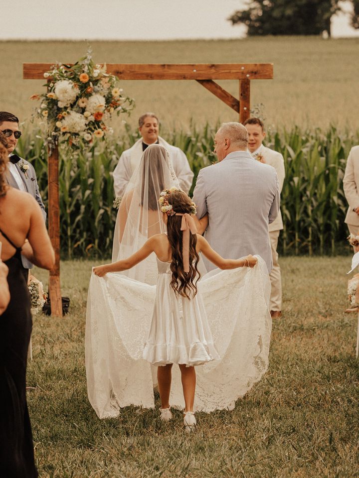 Flower girl with pastel flower crown carries bride's train