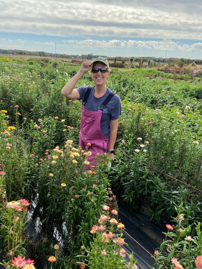 Liza stands in a field with a baseball hat and sunglasses.