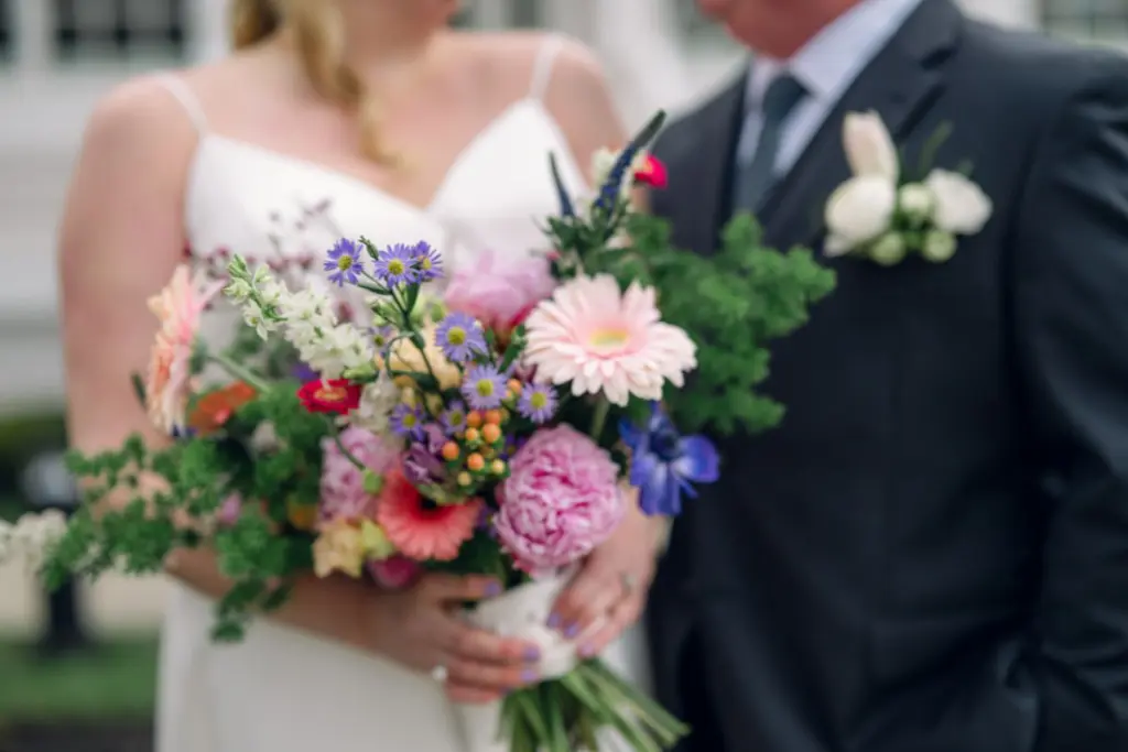 Bride holds colorful wedding bouquet and groom wears traditional pocket square boutonniere 