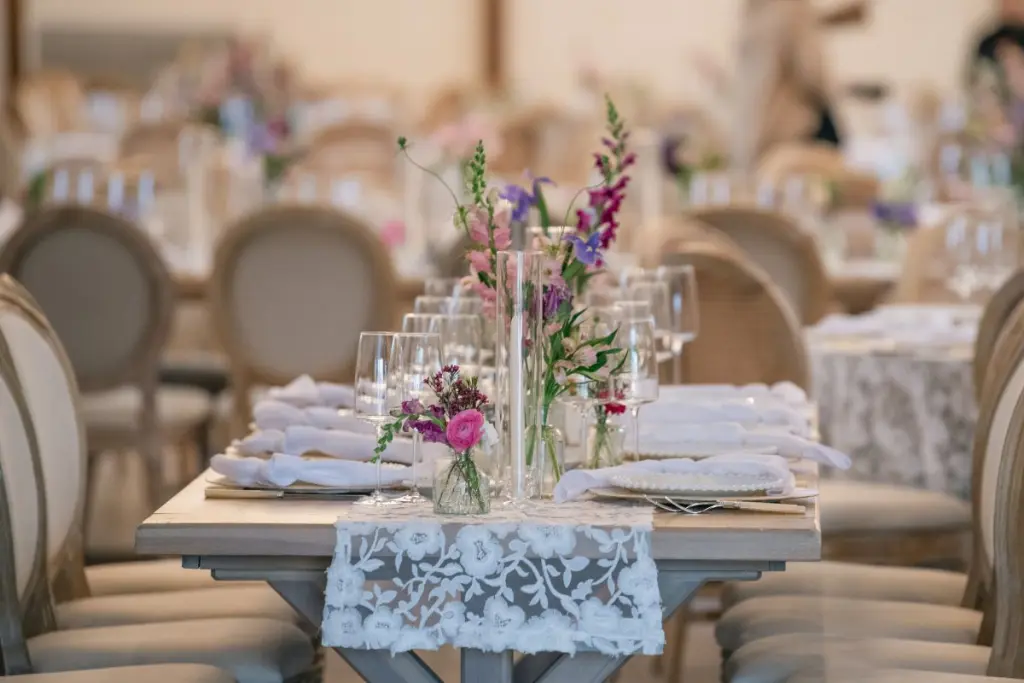 Rectangle table at wedding reception with lace linens and scattered vases with colorful flowers