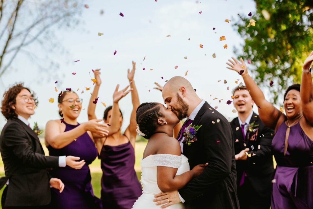 Bride and Groom kiss under tossed dried flower petals.