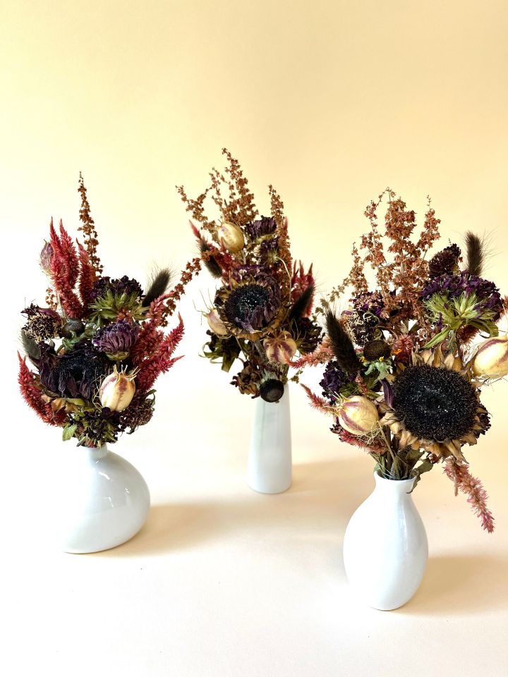 Three white bud vases with dark moody floral arrangements.