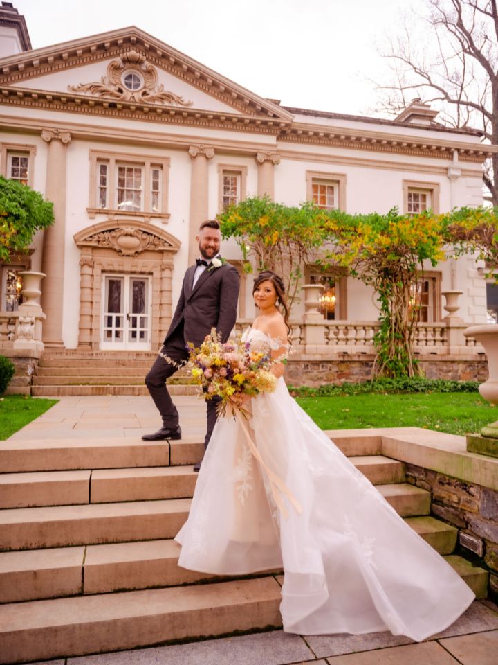 Bride and groom pose on mansion steps.