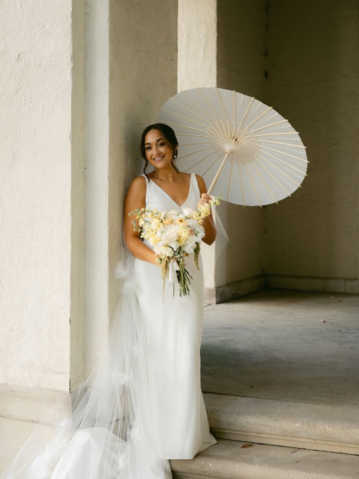 Bride holds a white parasol and flower bouquet.