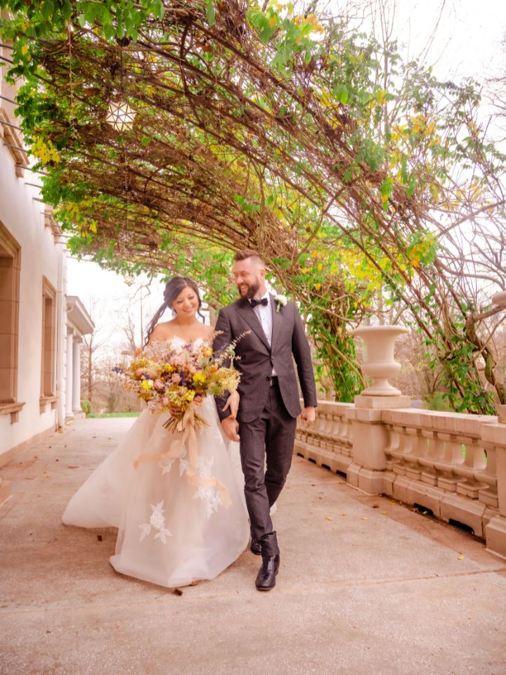 Bride and groom walk under a greenery ceiling.