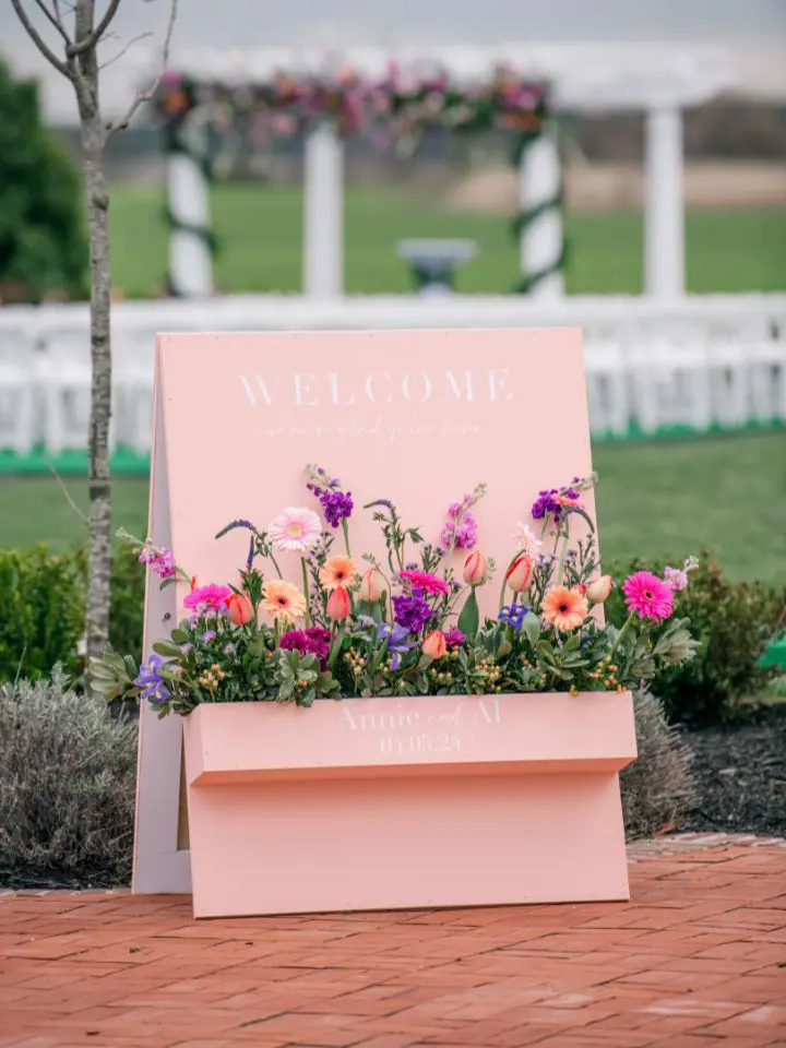 A unique wedding welcome sign with a flower box filled with bright colorful wedding flowers