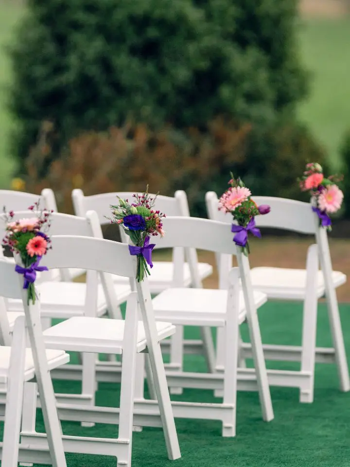 White folding chairs for wedding ceremony with flower bundles tied to the chairs along the aisle