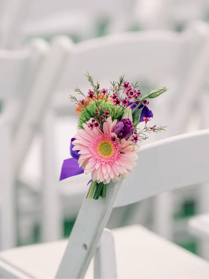 Close up of pink and purple flowers tied with purple ribbon to white chairs at wedding ceremony