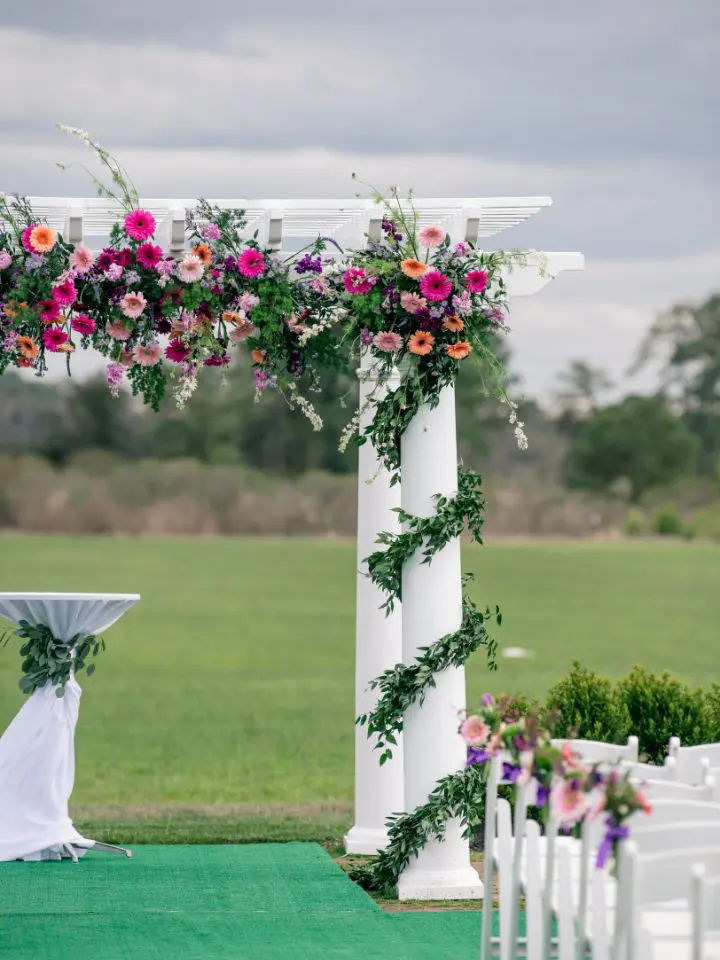 Greenery wrapped around columns and a large bright colored oasis garland wrapped along the top of the wedding arch