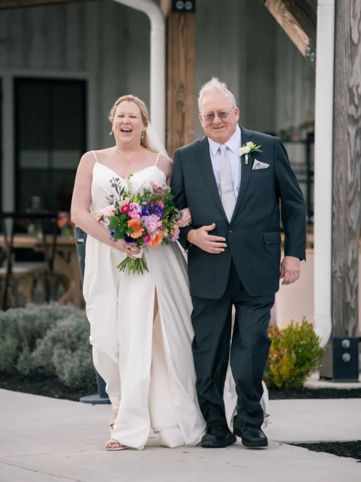 Bride walks down the aisle with her father both wearing beautiful flower personals