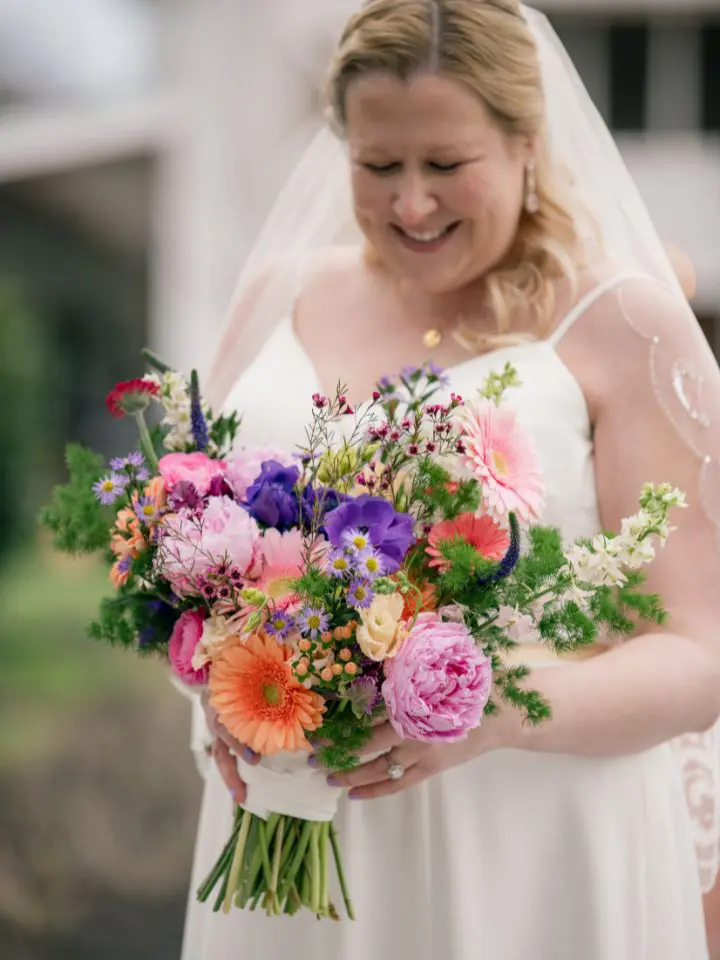 Annie, the bride, smiles as she holds her brightly colored wedding bouquet wrapped with fabric from her wedding dress