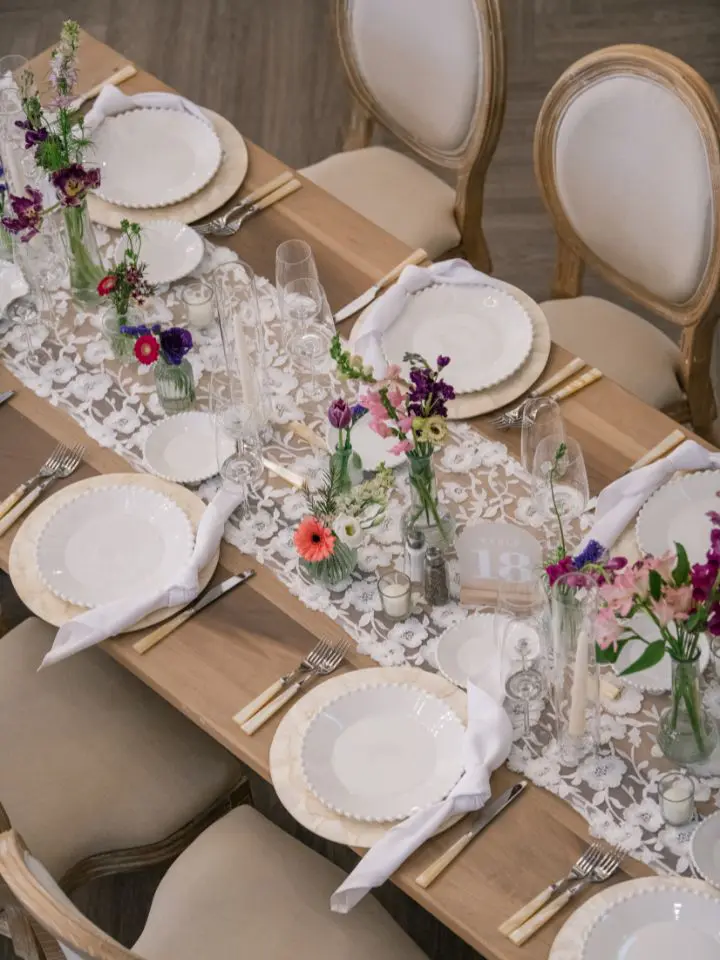 Fancy lace linens on rectangle guest table with scattered flower vases