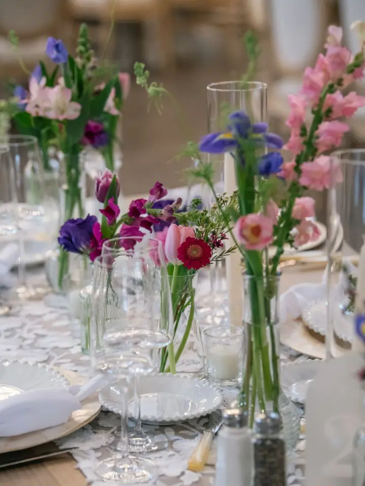 Scattered flower vases on guest tables for colorful wedding reception